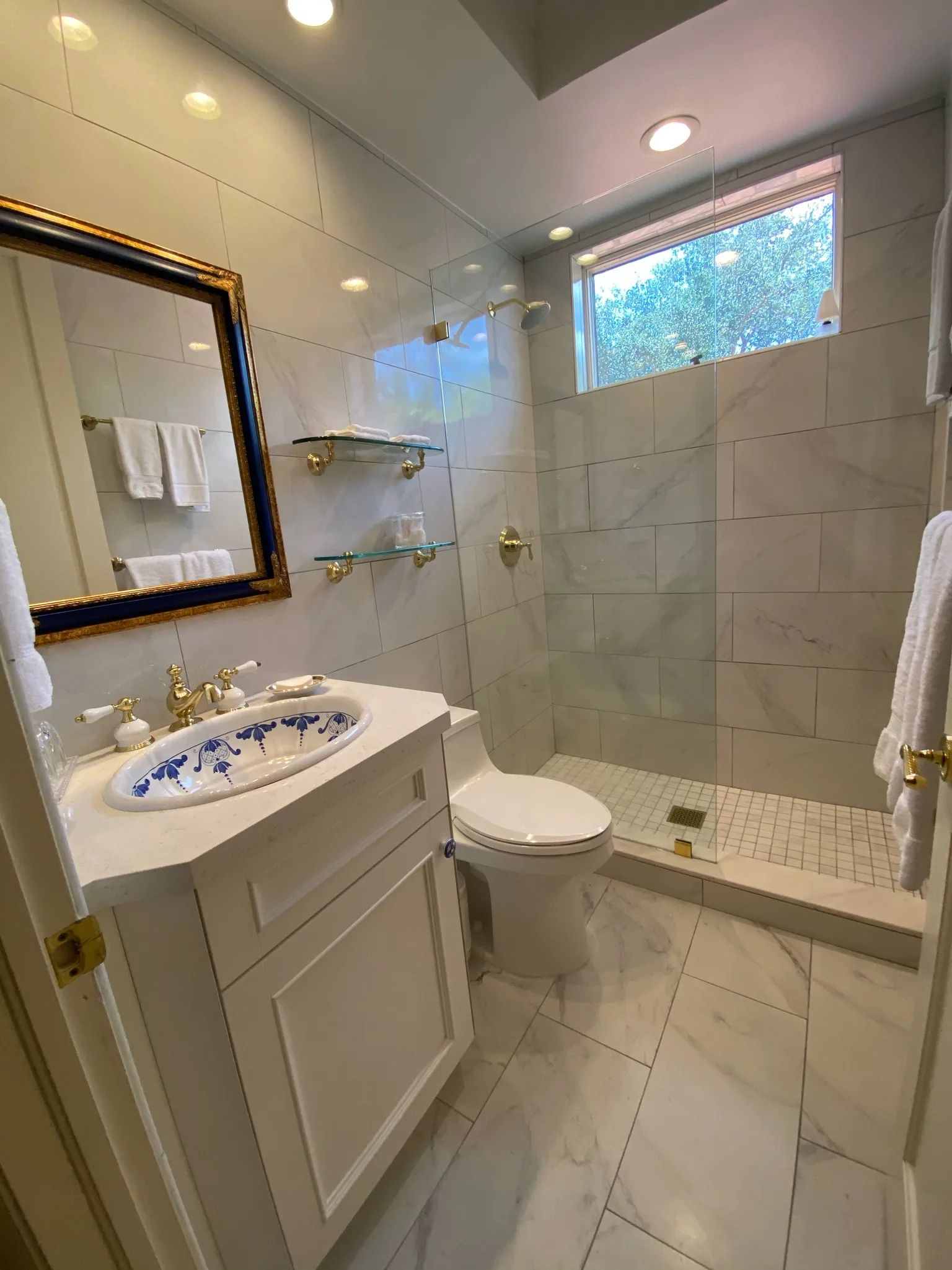 Bath with marble walls and an arched mirror — Casa de Marbella, Palm Beach Gardens, FL