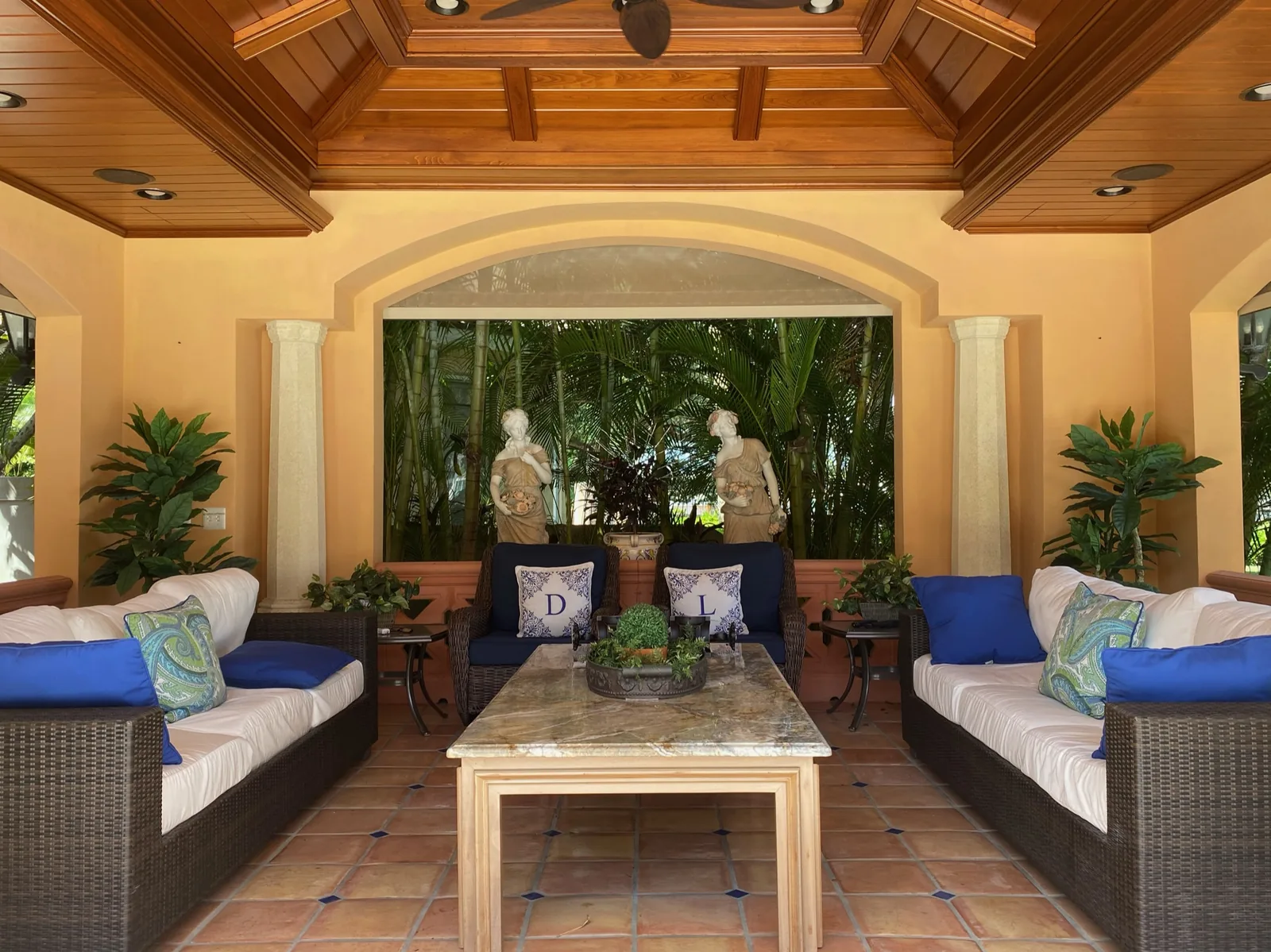Covered patio with wicker seating and garden sculptures — Casa de Marbella, Palm Beach Gardens, FL