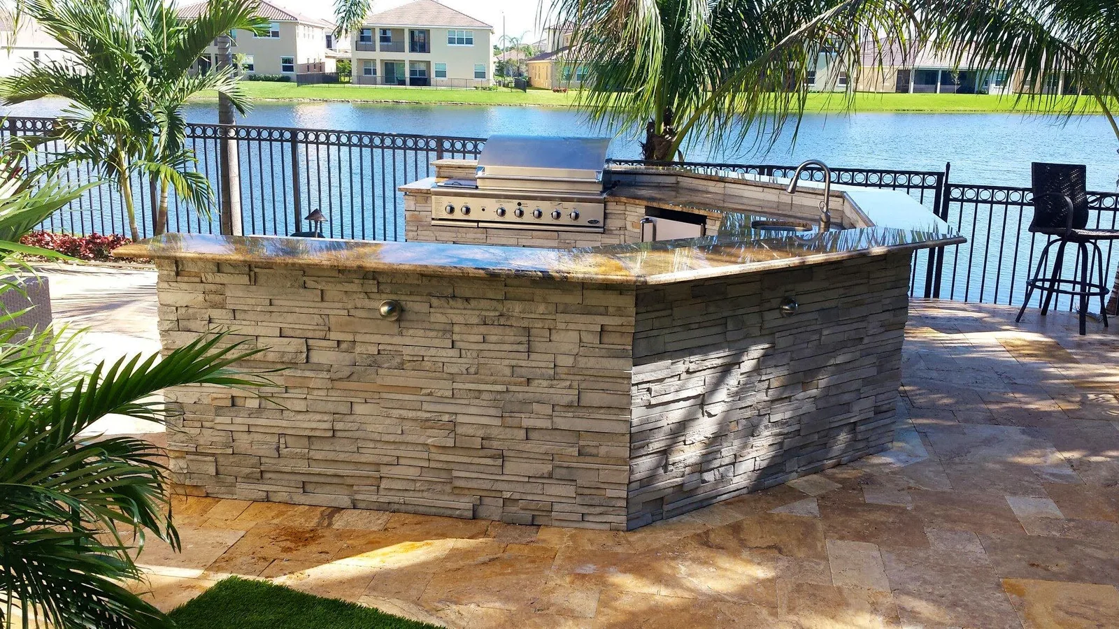 Outdoor kitchen with a stone island on a lakefront patio — Olympia, Wellington, FL
